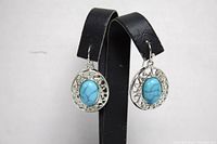 Pair of drop earrings shown from the front, each featuring a blue oval inset stone framed by silver-toned metal with intricate detailing.