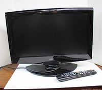 Front view of the Coby 19 inch LCD TV with DVD player, showing the screen and base stand with coiled cable placed in center, along with remote control placed in front.