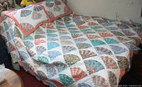 Quilt with multicolored fan patchwork pattern spread on bed, showing full size and design, with coral border visible