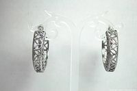 Front view of both silver tone hoop earrings with intricate lacey cut-out design displayed on a clear stand.