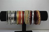 Full view of gold and silver tone bangles arranged on a display stand showing a variety of designs, some with rhinestones and some with enamel and etched patterns.