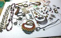 Full display of assorted costume jewelry spread on table including bracelets, necklaces, earrings, rings, and clips in mixed styles and colors.