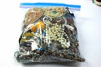 Large sealed zip lock bag filled with assorted broken costume jewelry pieces including beads, chains, and brooches.
