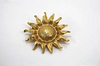 Front view of gold tone sunflower brooch showing textured petals and central disk, lying flat on a white background.