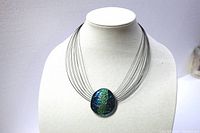 Full view of the multi wire silver tone necklace on display bust, showing the large oval enamel pendant with green shades in center.