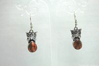 Front view of both orange brecciated jasper earrings with butterfly decorations hanging on display stand.