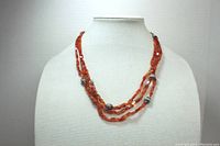 Overall view of the orange sphalerite triple strand necklace displayed on a mannequin bust, showing the length and drape of the necklace.