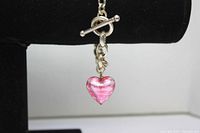 Close-up of the pink glass rose heart charm attached to the sterling silver bracelet with toggle clasp against black display stand.