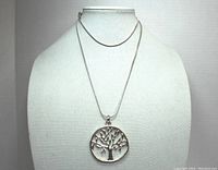 Full view of silver toned tree pendant necklace on display bust showing chain and pendant.