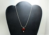 Full view of sterling silver chain with circular striped pendant and bead on display stand