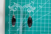 Pair of black onyx drop earrings displayed on clear stand with measurement grid background to verify length.