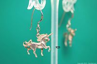 Close-up of one sterling silver unicorn earring hanging from a clear stand, marked 925 on the ear piece.