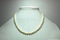 Full view of the pearl necklace displayed on a gray-white textured bust, showing the full 18-inch length with pearls evenly spaced.