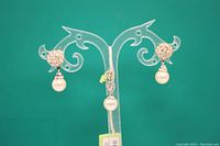 Pair of rhinestone pearl earrings displayed on clear earring stand against green background.