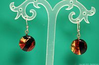 Front view of red, black, and yellow disc earrings hanging on a display stand showing round discs and sterling silver hooks.