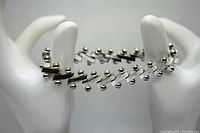 Front view of the sterling silver bracelet demonstrating the angled bars and ball design placed on a white display hand.