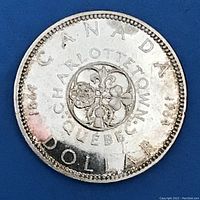 Reverse side of the 1964 Canadian Silver Dollar displaying a floral design surrounded by the text 'CANADA', 'CHARLOTTETOWN', 'QUEBEC', and the years '1864' and '1964'. The coin shows light wear and minor discoloration.