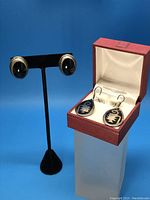 Two pairs of sterling silver earrings displayed; large teardrop-shaped dangle earrings with black onyx and smaller oval onyx studs on black stand.