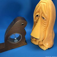 Both money banks shown side by side on blue background, highlighting the wooden beaver with visible coin compartment and yellow sad hound dog bank