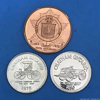 Photo showing one copper-colored medallion from Kent Coin Club from 1973, front with maple leaf and club crest labeled 'Tenth Anniversary'. Two silver-colored trade dollar coins from 1875 and 1890 from Chatham Ontario with vintage carriage and wagon imagery on front.