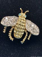 Front view of the Kenneth J Lane crystal queen bee brooch showing clear crystals on the wings, yellow crystals on the body, and blue crystal eyes on a gold-tone metal base.