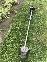 Full length photo of the Husqvarna Mondomax string trimmer on grass showing shaft, handle, and cutting head shield.