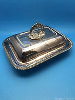 Closed view of the large covered silver plate serving dish showing the ornate handle on lid and detailed rim.