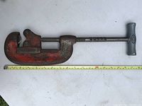 Full view of the large pipe cutter next to a measuring tape showing approximately 18 inches in length and a wide handle for turning.