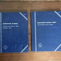 Two blue hardcover coin folders side by side on wood surface, one titled Canadian Nickel Collection 1922-1960 Number One and the other Canadian Small Cent Collection 1920 to Date