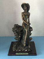 Front view of the Renaissance Collection bronze finish seated lady figurine on wooden base, showing details of the dress, hat, floral background, and plaque.