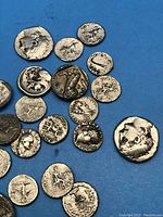 Top down view of multiple replica Roman coins scattered on blue background showing various designs including portraits and animals.