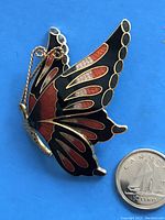 Butterfly brooch shown flat with a Canadian dime for size reference, showing detailed enamel pattern and gold tone edges with an attached safety chain.