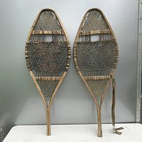 Full view of pair of vintage snowshoes showing wooden frames and woven cord netting with wear and damage