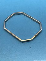 Angular geometric sterling silver bracelet laid flat on blue background, showing hinged clasp open and closed positions.
