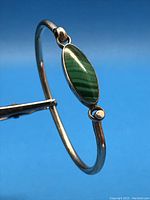 Bracelet view showing oval green malachite stone set in silver with a hinged top detail and band.