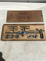 Open wooden box with visible tools neatly arranged inside showing dies, taps, tap wrench, and die holder