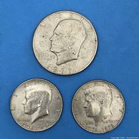 Obverse side of the three coins showing profiles: 1971 Eisenhower dollar on top, two 1976 Kennedy half dollars below.