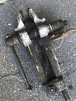 Large vintage blacksmith post leg vise with a long tail, laid on asphalt surface.