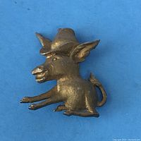 Front view of the gold-tone donkey brooch with a hat on blue background.