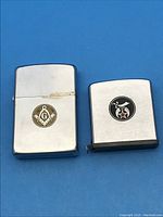 Two Zippo items side by side on blue background: a lighter with Masonic emblem and a tape measure with Shriners emblem