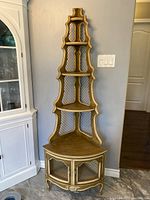 Full view of the beige and brown wooden corner cabinet with wire mesh backing, glass panel doors, tiered shelves, and curved legs against a grey wall.