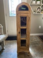 Closed view of the small wooden curio cabinet showing rounded top glass panel and wooden lower door with glass panes.