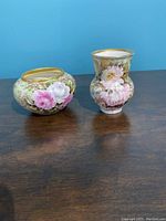 Photo showing small hand painted Limoges porcelain vase and round bowl with floral decorations and gold trimmed edges on a wooden table against blue background.