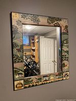 Full view of the folk art mirror showing landscape paintings all around the frame and reflective mirror in the center.