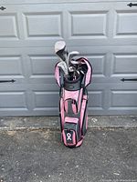 Photo of ladies right-handed golf clubs in pink and black golf stand bag with multiple zippered pockets and club head covers in front of garage door