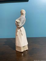 Front view of the porcelain figurine showing a girl holding a lamb, against a blue background.