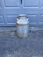 Front view of vintage Dominion Dairies metal milk can showing embossed lettering, handles, and natural weathering.