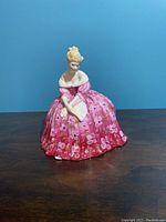 Photo of the full Royal Doulton porcelain figurine 'Victoria', showing the detailed pink floral dress and seated woman holding a fan.