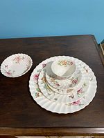 Photo showing a 6-piece place setting of floral Royal Doulton Clovelley china on a dark wood surface with cup, saucer, dessert plate, salad plate, dinner plate, and bowl.