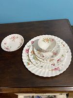 Set of 6 pieces displayed including plates, cup, saucer, and bowl on wooden table showing floral pattern and scalloped edges